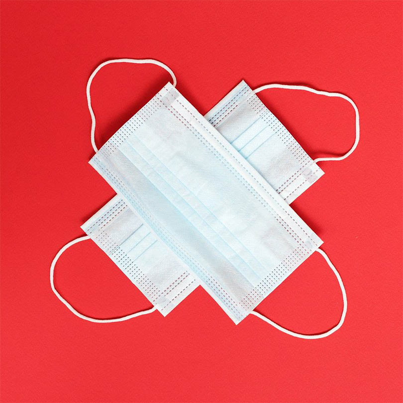 Dos mascarillas quirúrgicas cruzadas sobre una superficie roja